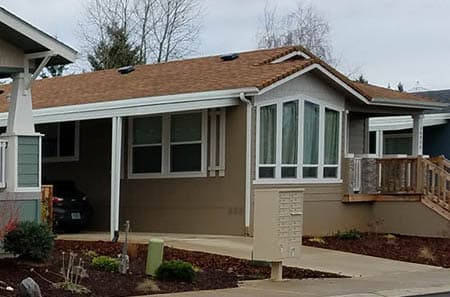 Manufactured home with carport, patio, and a big bay window located in in a manufactured home community.